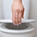 hand of a man closing the lid of a toilet