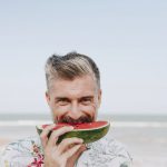 Mature man eating watermelon at the beach